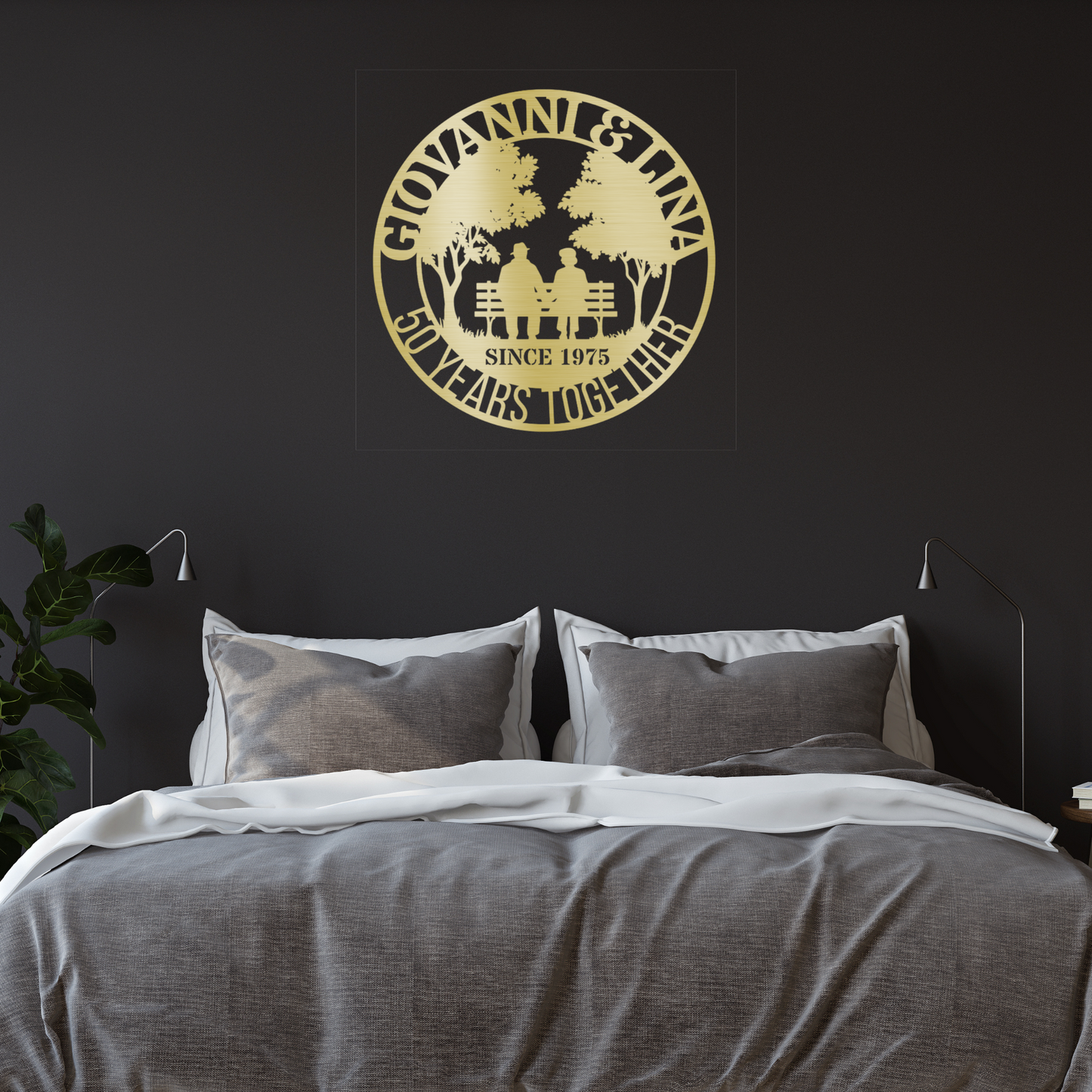 A cozy bedroom features a neatly made gray and white bed. Above, the Personalized 50th Wedding Anniversary Metal Wall Art from MEM Design Studio displays "GIOVANNI & LINA 50 YEARS TOGETHER SINCE 1975" with a couple sitting on a bench.