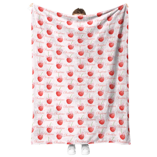 Someone holds a Custom Coquette Cherry Bow Seamless Pattern Fleece Blanket featuring "Christine" and red apple illustrations, offering a girly cottagecore aesthetic.