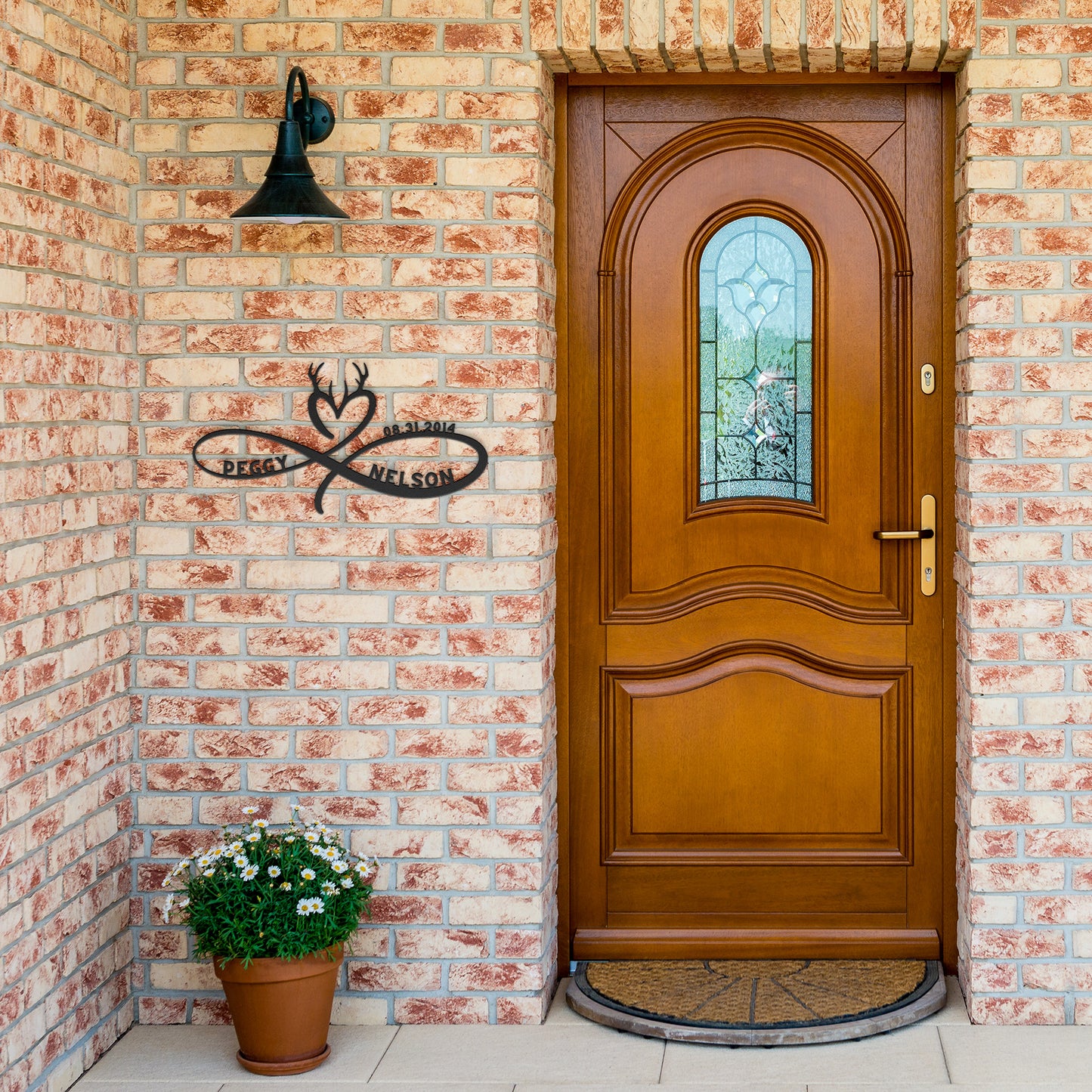 A wooden door with a decorative glass panel is set in a brick wall. A potted plant sits on the doorstep. The names "Peggy" and "Nelson" are elegantly displayed on a Personalized Infinity Love Heart Metal Sign For Hunting Couples, crafted from durable 18 gauge steel.