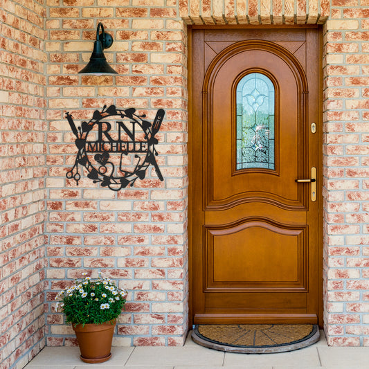 A wooden door with a glass panel is set in a brick wall. A potted plant is on the ground, and a decorative 18 gauge Personalized Nurse Metal Sign with intricate designs is mounted to the wall next to the door, adding a touch of elegant home decor.
