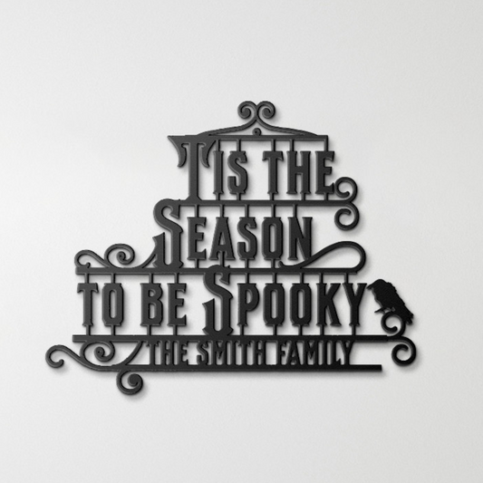 A brick wall with a wooden arched door and a Custom Halloween Metal Sign reading "Tis the season to be spooky." A potted plant with white flowers is placed on the left side of the door.