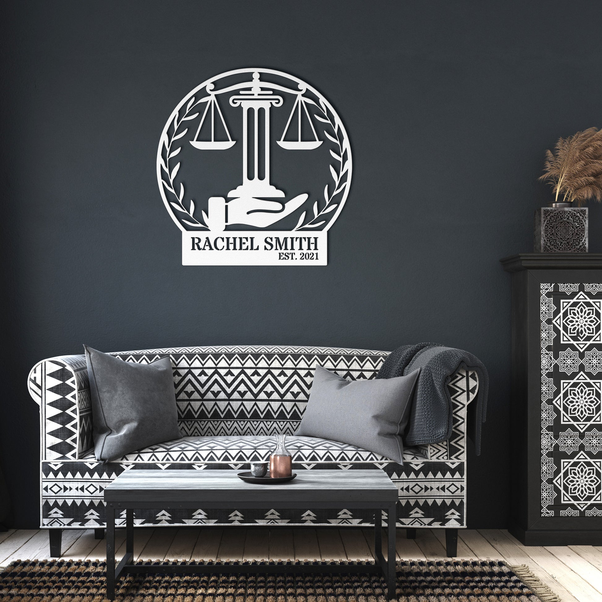 Living room featuring a patterned black and white sofa, pillows, and the Scales of Justice Metallic Wall Art with the text "Rachel Smith, Est. 2021," adding a sleek touch to your home decor.