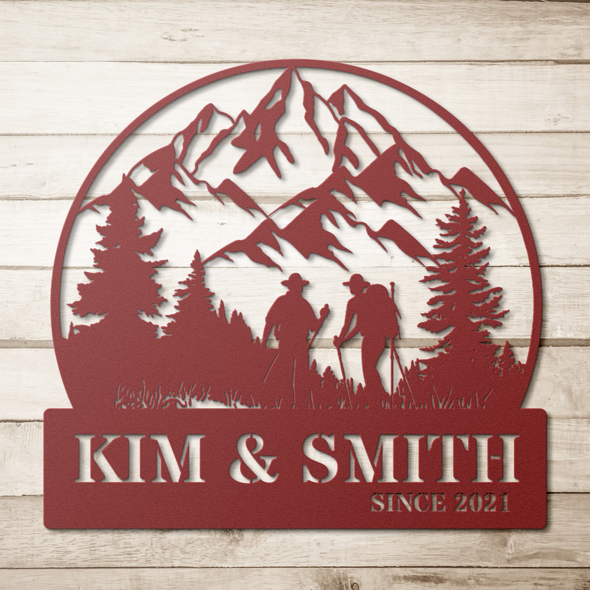 A brick house exterior with a wooden door, arched stained glass, wall-mounted lamp, potted flowers, and an 18 gauge steel decor sign reading "Kim & Smith," featuring the Updated Hiking Couple Metal Art with a mountain and tree silhouette that serves as a timeless piece of home decor.