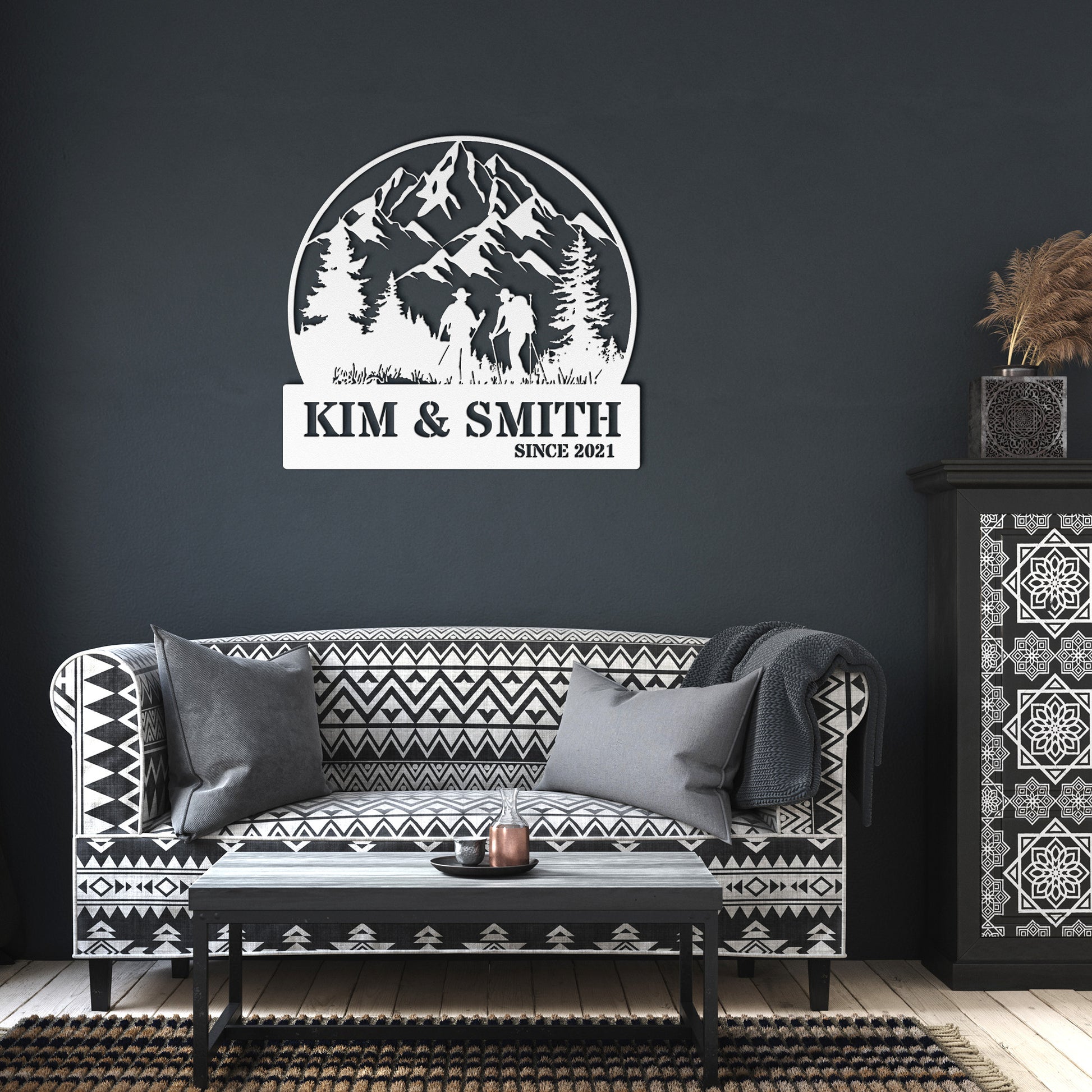 A brick house exterior with a wooden door, arched stained glass, wall-mounted lamp, potted flowers, and an 18 gauge steel decor sign reading "Kim & Smith," featuring the Updated Hiking Couple Metal Art with a mountain and tree silhouette that serves as a timeless piece of home decor.