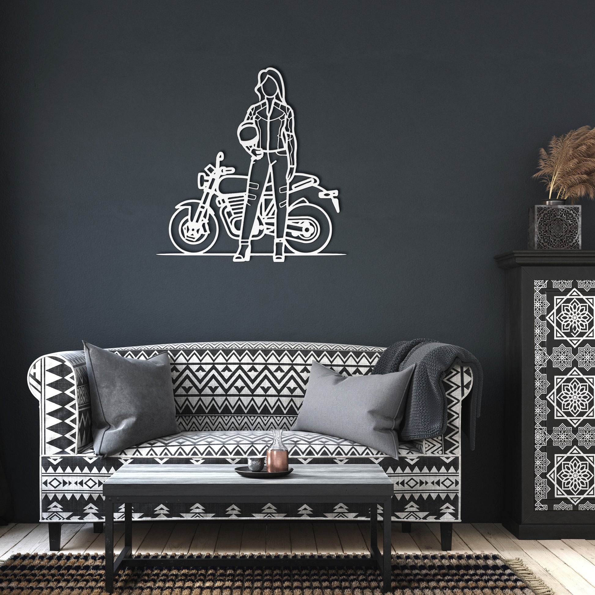 Living room with a patterned sofa, a decorative black and white metal sign titled "Woman Biker," and a black table with pillows.