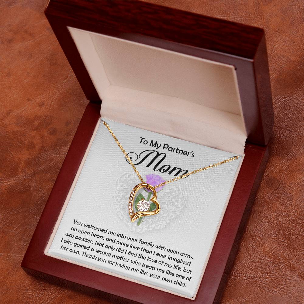 The Partner's Mom-A Second Mother - Forever Love Necklace, with a gold finish and sparkling cubic zirconia, rests in an open wooden box. A card inside reads: "To My Partner's Mom" with a heartfelt message of gratitude and love.