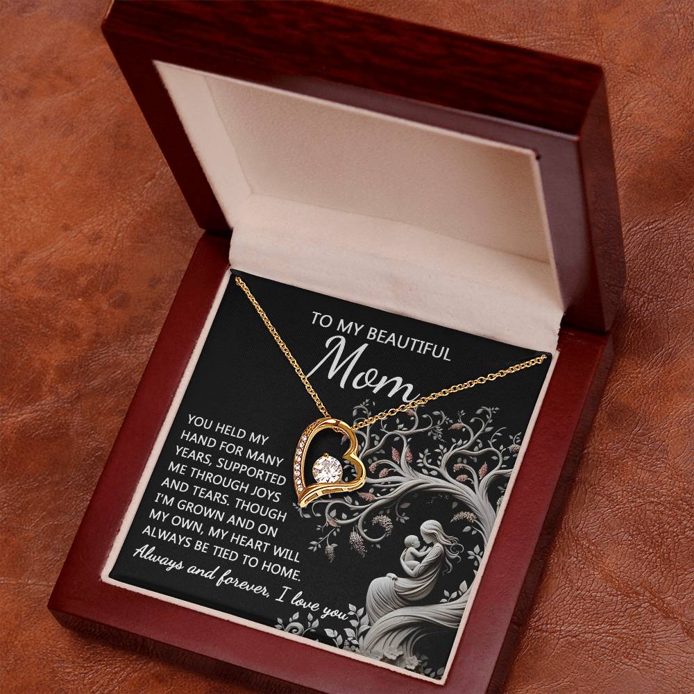 The "To Mom, On My Own - Forever Love Necklace" features a gold heart-shaped pendant adorned with a central cubic zirconia stone. It is elegantly presented inside a wooden box, which includes an inscription on the interior lid to "Mom," expressing love and appreciation—making it the perfect personalized gift.