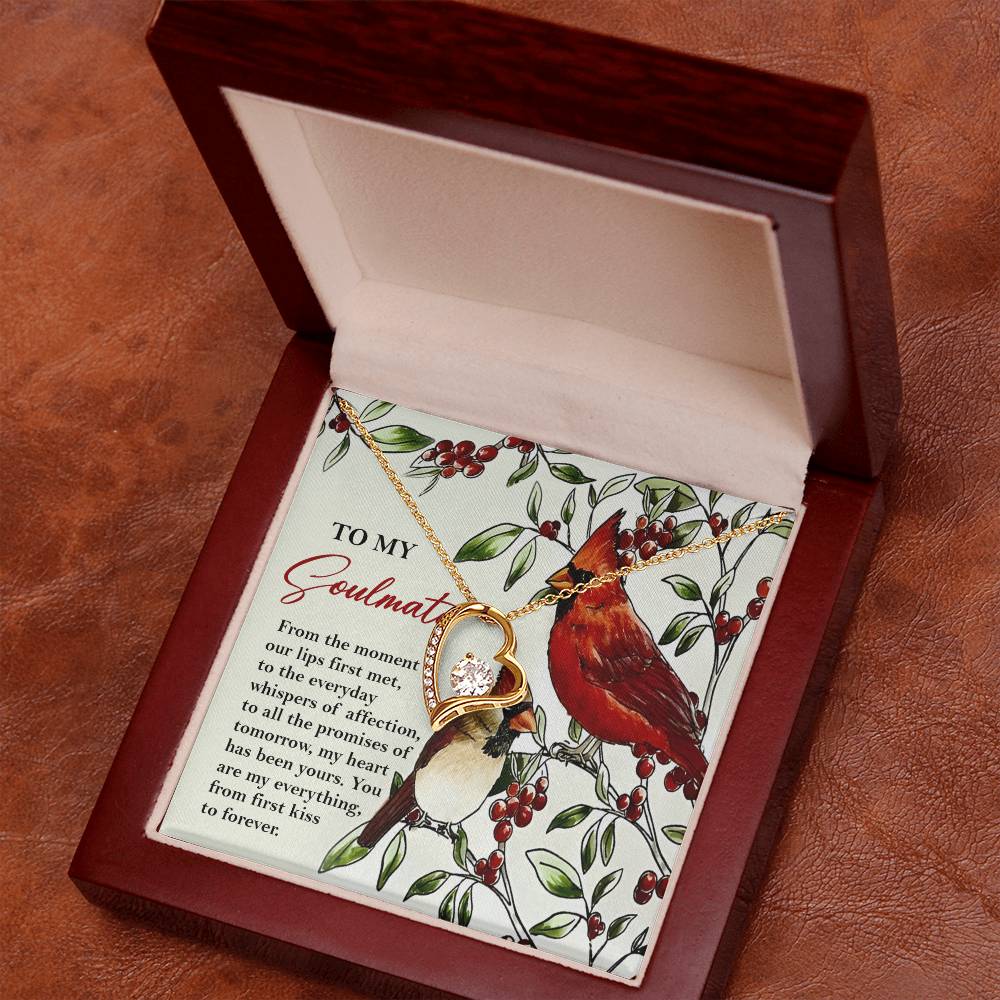 The Soulmate-First Kiss - Forever Love Necklace features two interlocking rings and a dazzling CZ crystal pendant with a gold finish. It is packaged in a wooden box accompanied by a card that showcases a cardinal and includes a heartfelt love message.