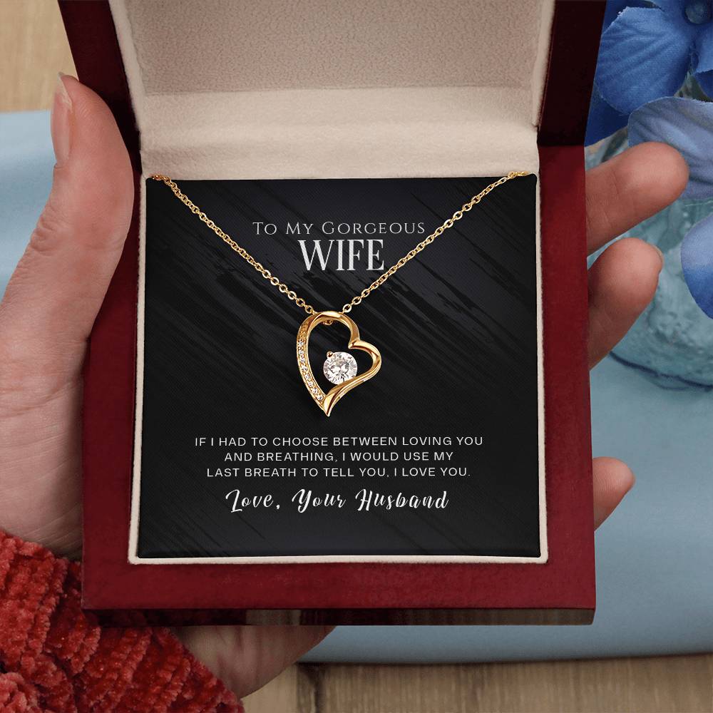A heart-shaped ShineOn Fulfillment cubic zirconia necklace with an engraved love message for a wife, presented in an open box held by a person.