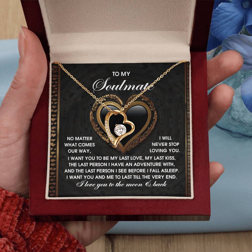 A hand cradles a box containing the Soulmate-The Very End - Forever Love Necklace, showcasing a gold heart with cubic zirconia stones. Inside, an inscription about love and soulmates complements the elegant piece, beautifully finished in 14k white gold.