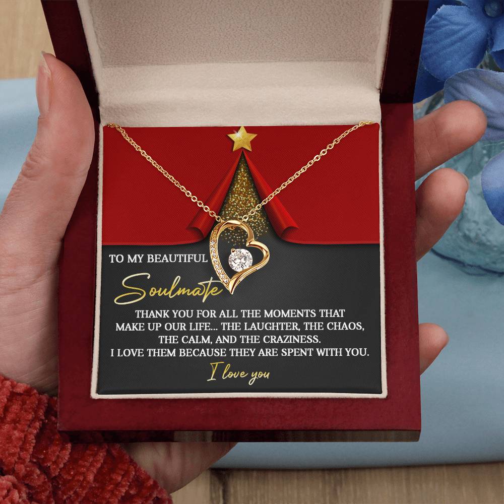 An open jewelry box, held in a hand, showcases the Soulmate-The Moments - Forever Love Necklace, which features a heart shape and is embellished with CZ crystals and a white gold finish. Inside the box, a decorative card conveys a heartfelt message of gratitude and love for a soulmate.