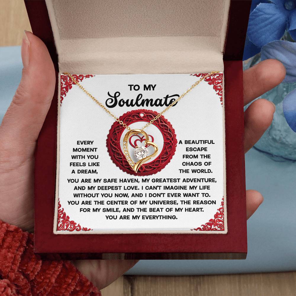 A hand holds an open box revealing the Soulmate-Like A Dream - Forever Love Necklace, adorned with heart-shaped pendants and shimmering cubic zirconia stones. This cherished gift is accompanied by a decorative card with a heartfelt message to a soulmate.