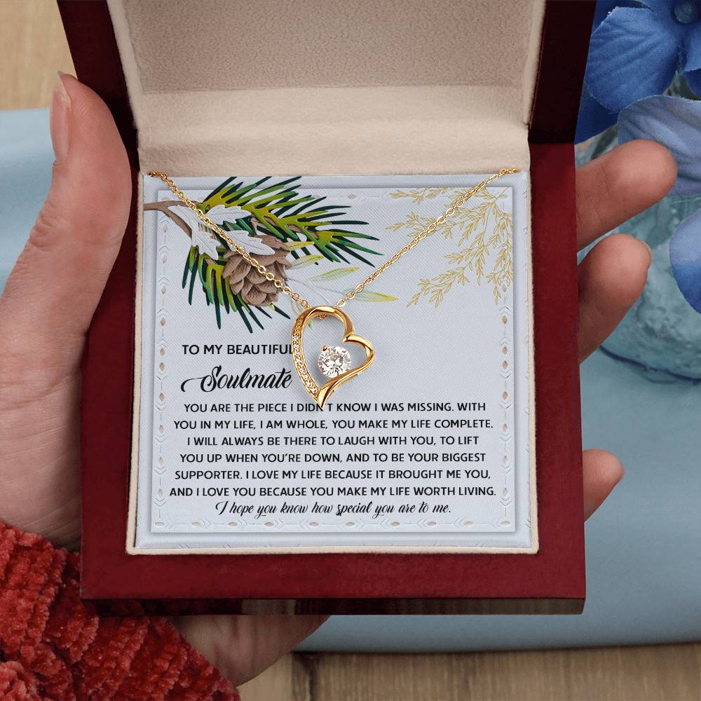 A person holds an open jewelry box showcasing the Soulmate-Biggest Supporter - Forever Love Necklace, embellished with a sparkling cubic zirconia heart. Inside the elegant gold-finished box, a heartfelt message about a soulmate is visible. Nearby, partially seen blue flowers enhance the romantic atmosphere.