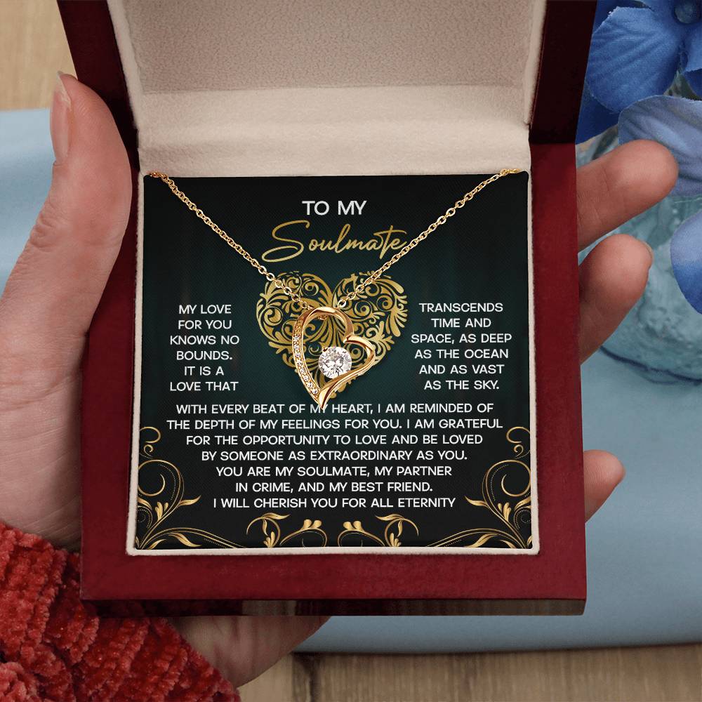 A person holds an open jewelry box with a Soulmate-The Sky - Forever Love Necklace featuring a gold finish and heart-shaped designs, accompanied by a message card for their soulmate.