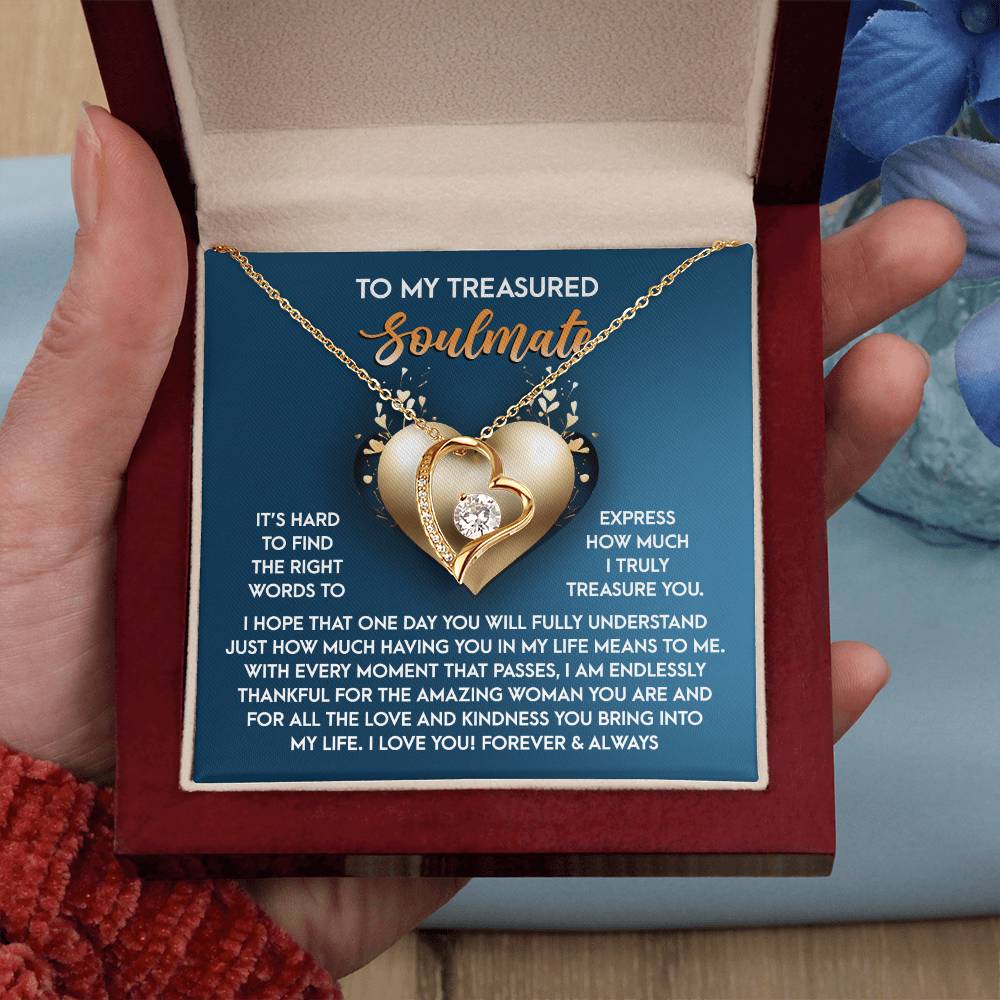 A hand holds a jewelry box displaying the Soulmate-In My Life - Forever Love Necklace, featuring a heart-shaped pendant with a dazzling CZ crystal glistening on its white gold finish. Inside, text beautifully expresses love and appreciation for your soulmate.