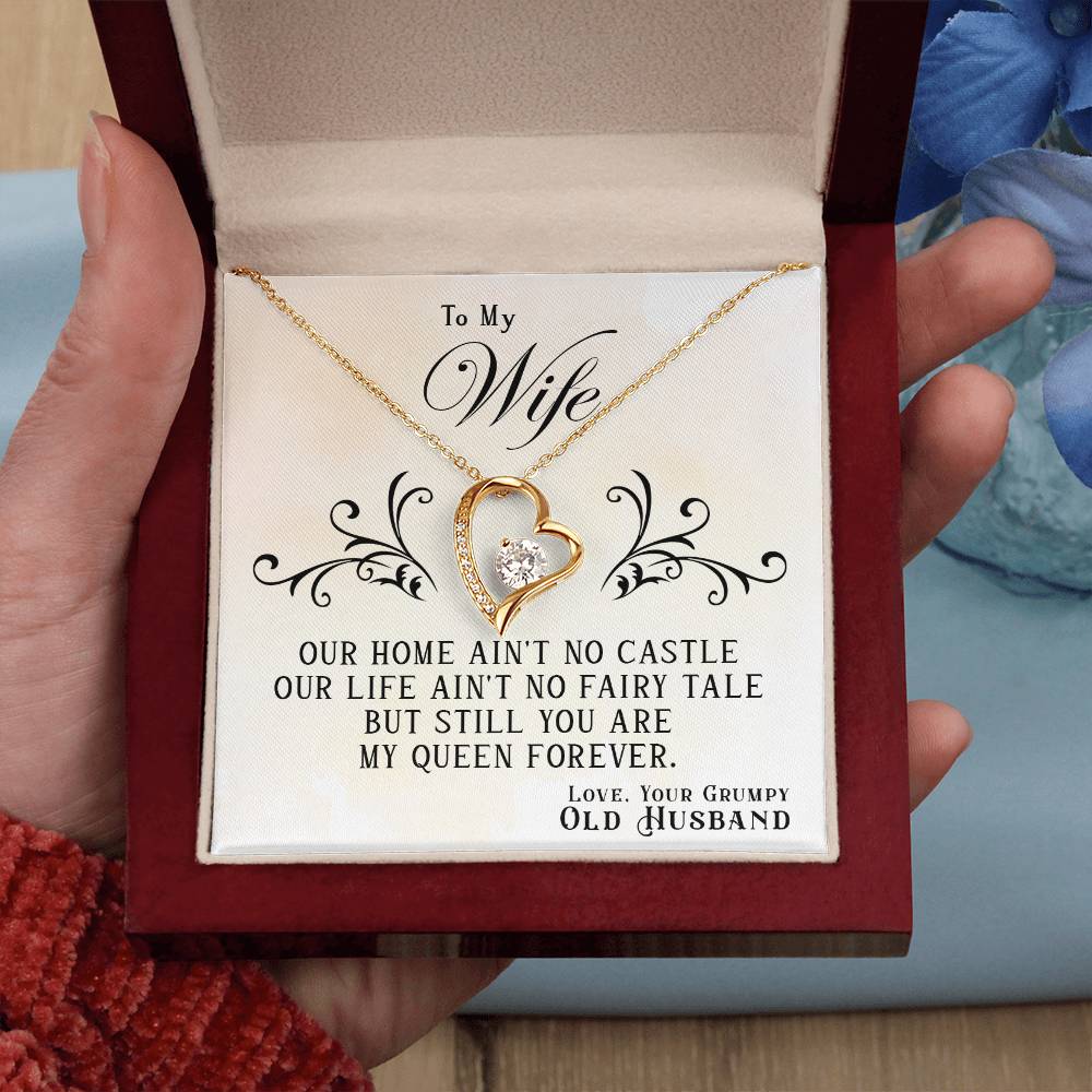 A hand holding a jewelry box with a To My Wife, You Are My Queen Forever - Forever Love Necklace from ShineOn Fulfillment featuring a gold finish and cubic zirconia, and a love note for a wife from her husband.