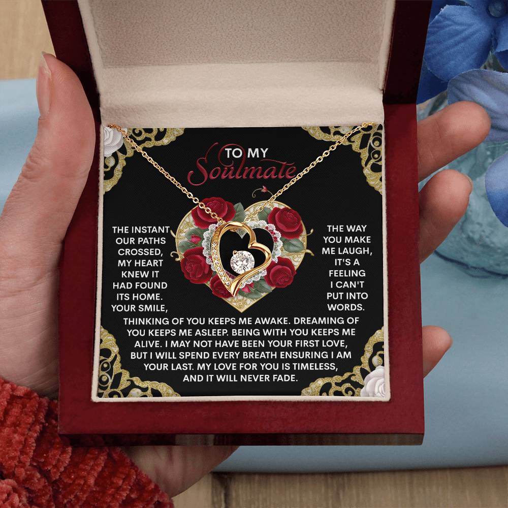 A person unveils the Soulmate-Never Fade - Forever Love Necklace in an open gift box. The heart-shaped pendant sparkles with CZ crystal and comes in white or yellow gold finish. Romantic text and ornate designs with red roses embellish the box's interior.