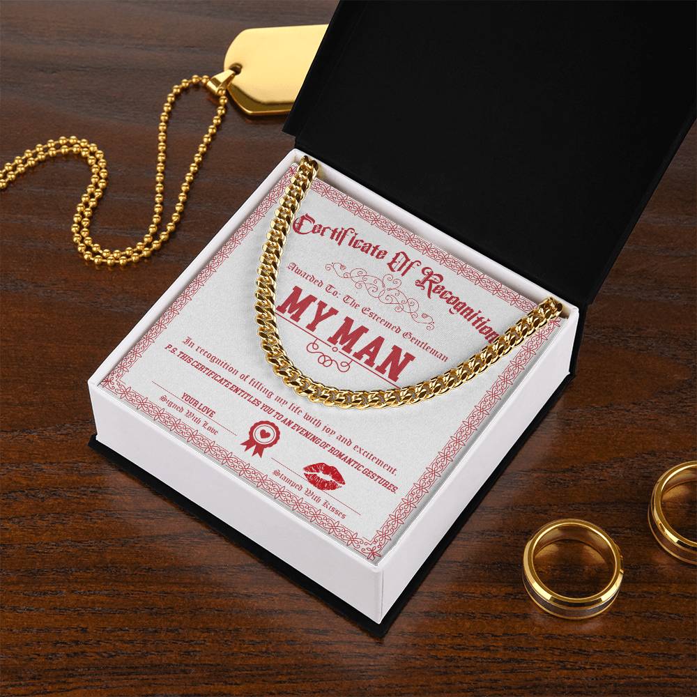 Open black box with a "Certificate of Recognition" titled "My Man-Esteemed Gentleman - Cuban Link Chain," featuring a 14K yellow gold chain necklace, two gold rings, and a polished stainless steel dog tag necklace on a wooden surface.