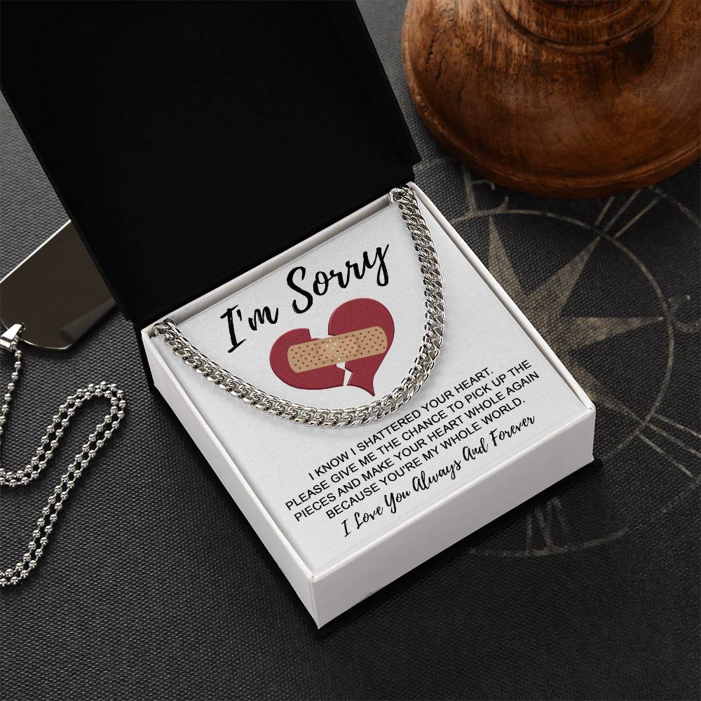 A Sorry-The Pieces - Cuban Link Chain on a black cushion inside a box that reads, "I'm Sorry," with an illustration of a broken heart and an apology note.