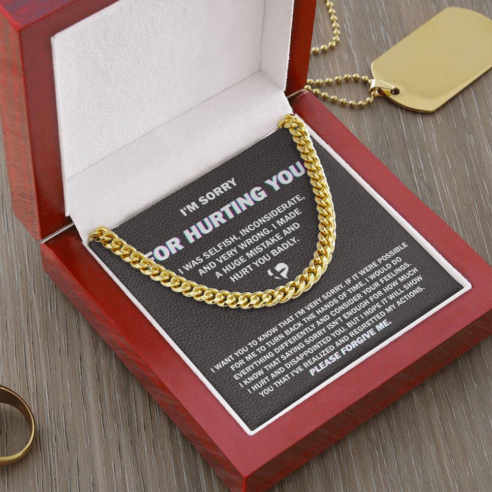 A gold "Sorry, Hurt You Badly - Cuban Link Chain" necklace displayed in an open red jewelry box. The interior of the box lid has a printed apology note that says "I'm sorry for hurting you," along with a detailed message expressing regret. A gold dog tag hangs on one side of the box, highlighting the necklace’s elegant design.