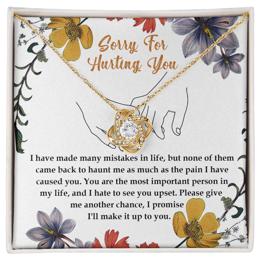 The Sorry-Haunt Me - Love Knot Necklace is a silver piece featuring an intertwined heart and infinity symbol adorned with cubic zirconia crystals, elegantly presented against a floral card that reads: "Sorry For Hurting You" with an apology message below.