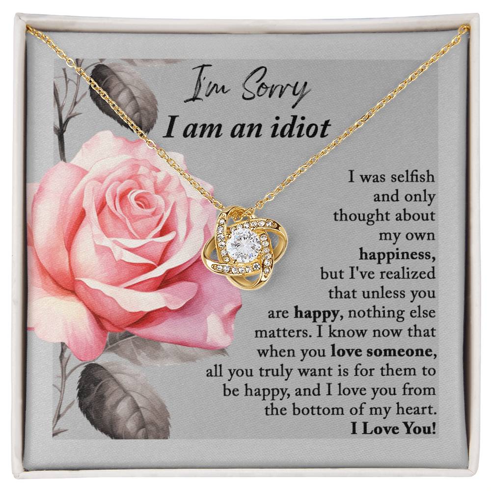 The "Sorry-Love Someone - Love Knot Necklace" is an elegant silver piece with a heart-shaped pendant, adorned with sparkling cubic zirconia crystals. It rests on a beautifully designed box featuring a pink rose and a heartfelt apology note, making it truly a classic gift.