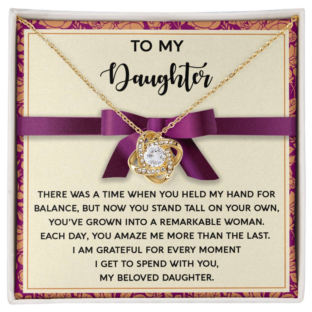 A box containing the Daughter-Spend With You - Love Knot Necklace in a beautiful yellow gold finish, accompanied by a touching message that reads, "To My Daughter... There was a time when you held my hand for balance, but now you stand tall on your own..." and followed by a heartfelt note.