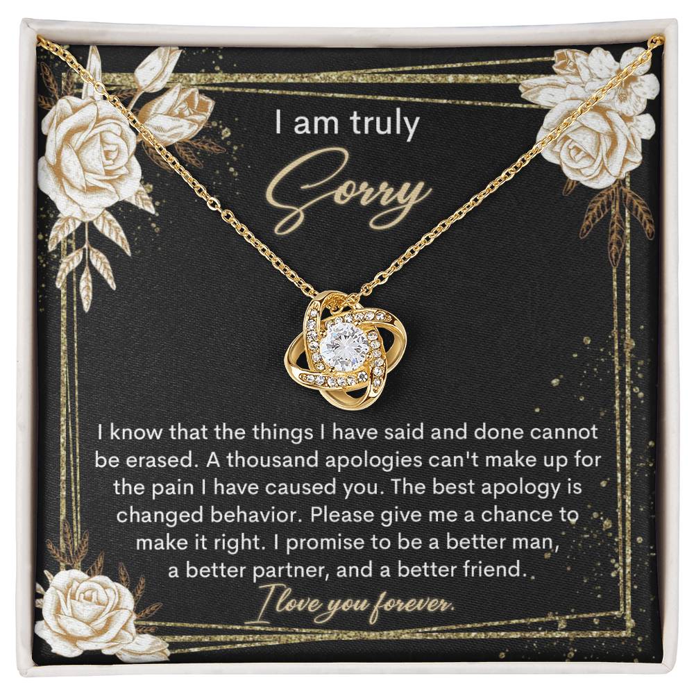 The Sorry-Cannot Be Erased - Love Knot Necklace, adorned with shimmering cubic zirconia crystals and available in a choice of white gold or yellow gold finish, is displayed against a backdrop of a black card bearing an apology message that reads, "I am truly sorry" and "I promise to be a better man, a better partner, and a better friend.