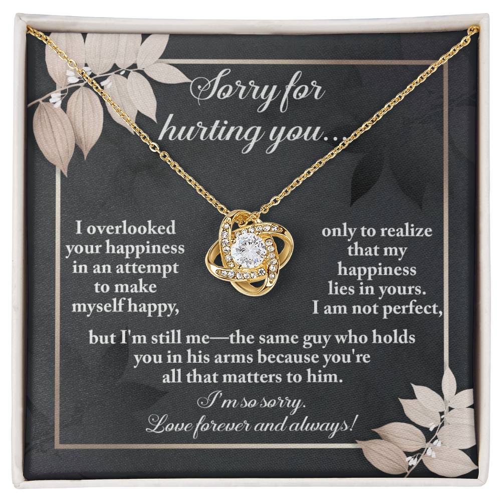 The Sorry-Lies In Yours - Love Knot Necklace, a stunning piece embellished with cubic zirconia crystals, is showcased against a dark-themed backdrop adorned with floral designs. The background beautifully conveys an apology message infused with love and regret.