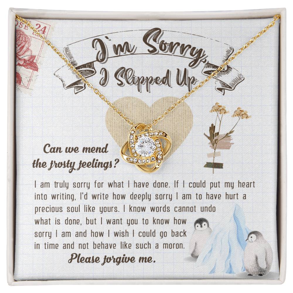 The Sorry-Precious Soul - Love Knot Necklace, featuring an intertwined heart pendant adorned with cubic zirconia crystals, is beautifully displayed in a box. The box comes with an apology note and charming illustrations of flowers, mail stamps, and penguins on a grid-patterned background.