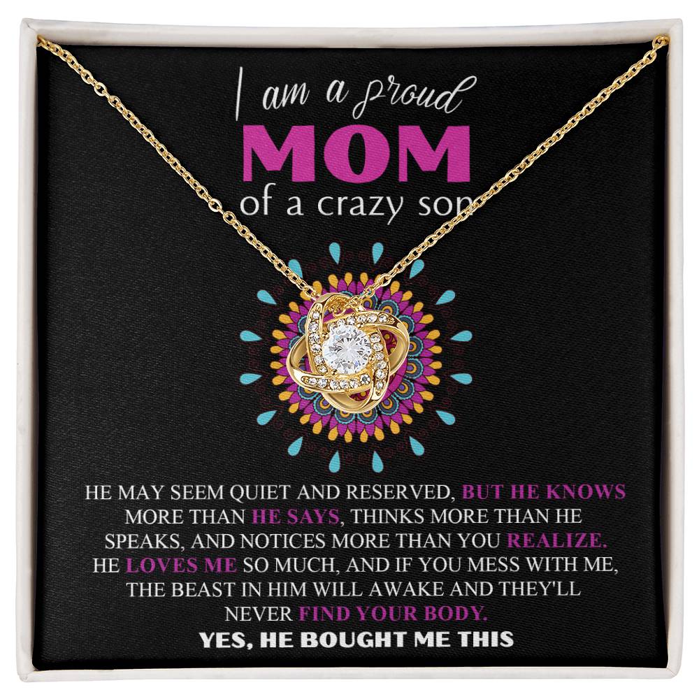 The "To Mom, Proud Mom - Love Knot Necklace" with a heart-shaped pendant is displayed in an elegant box. This 14k white gold piece boasts stunning cubic zirconia crystals. The box features a humorous message from a mother, highlighting her son's protective nature and how he lovingly purchased the necklace for her.