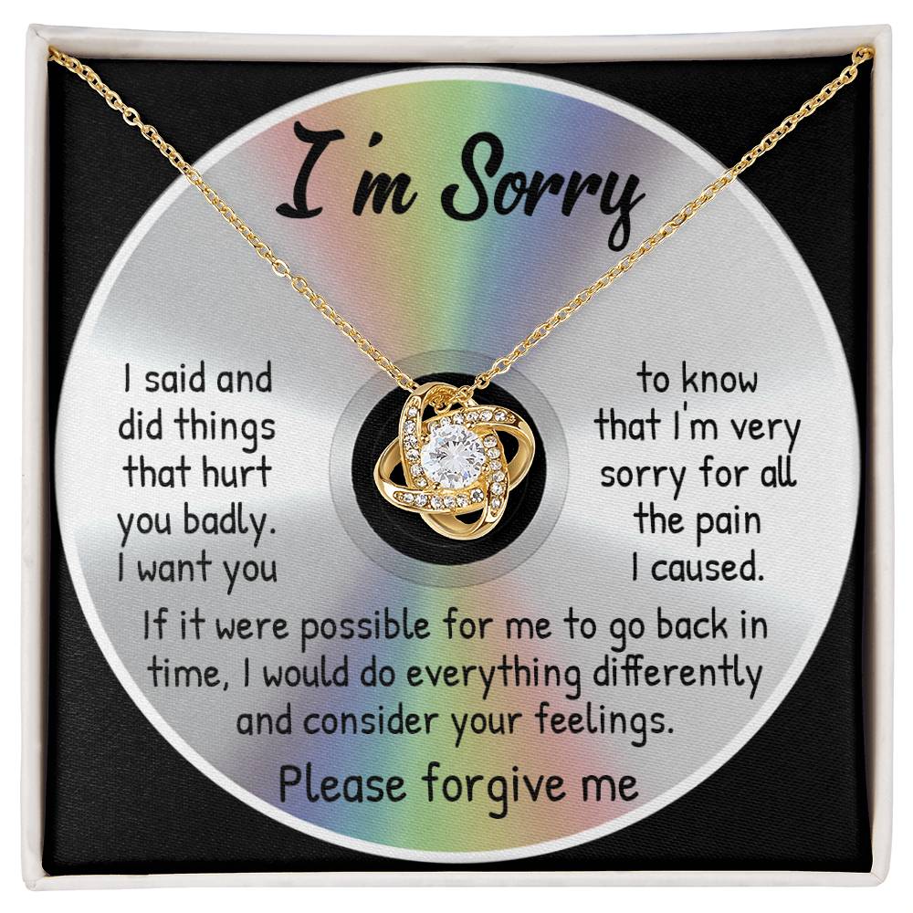 The "Sorry-Back In Time - Love Knot Necklace" features a circular pendant on a CD containing an apology message expressing regret for causing hurt and a heartfelt desire to make amends. The necklace boasts a stunning yellow gold finish adorned with cubic zirconia crystals, and the message concludes with, "Please forgive me.