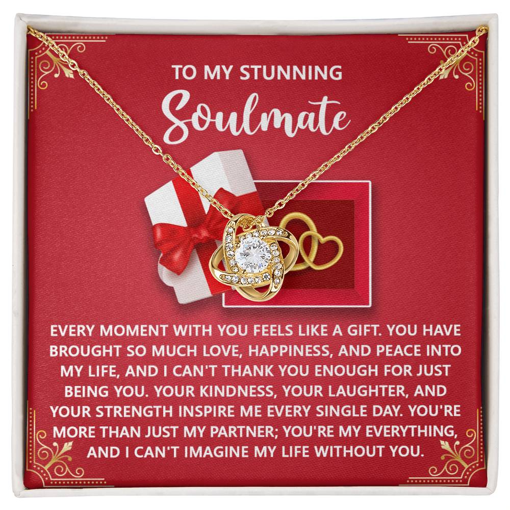 The Soulmate-Like A Gift - Love Knot Necklace showcases intertwined hearts, a central gem, and cubic zirconia on a red background. Paired with a heartfelt message for your soulmate, it's the perfect personalized gift expressing love and appreciation.