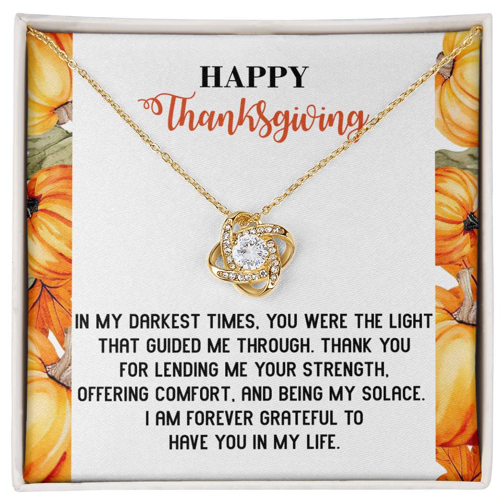 The Thanksgiving-Guided Me Through - Love Knot Necklace, featuring a gold heart-shaped pendant adorned with sparkling cubic zirconia crystals, rests elegantly on a "Happy Thanksgiving" card with an appreciation message and pumpkin decorations.