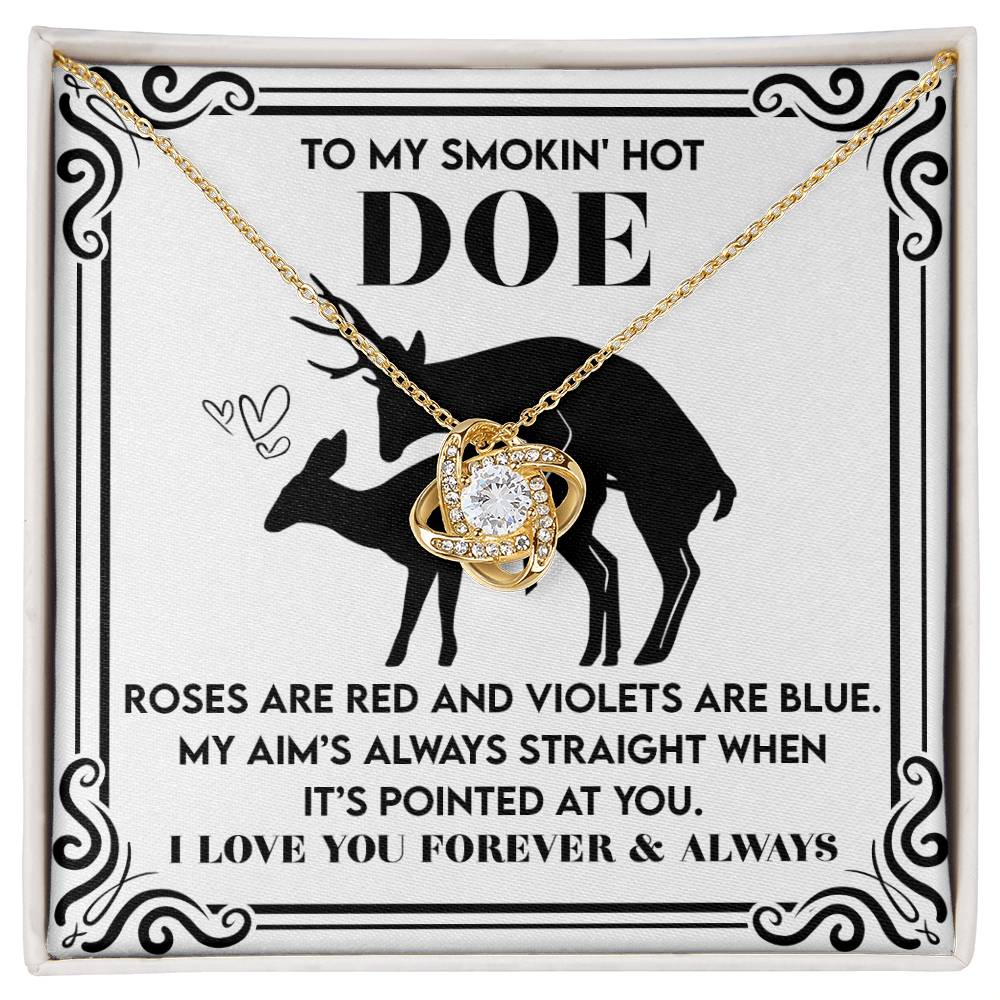 The Soulmate-Pointed At You - Love Knot Necklace features a gold finish heart pendant beside a cubic zirconia love knot, on a card saying "To my smokin' hot doe," with deer silhouettes and a sweet rhyming message of deep affection.