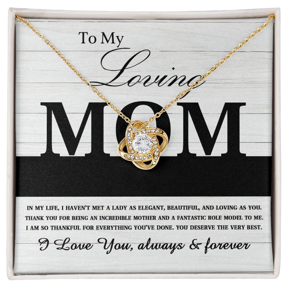 The "To Mom, Loving As You - Love Knot Necklace" is a gold piece featuring a pendant with a large central gem and smaller cubic zirconia crystals arranged in a four-leaf design. Presented on an appreciation card dedicated to "Mom," this necklace makes for an ideal personalized gift.