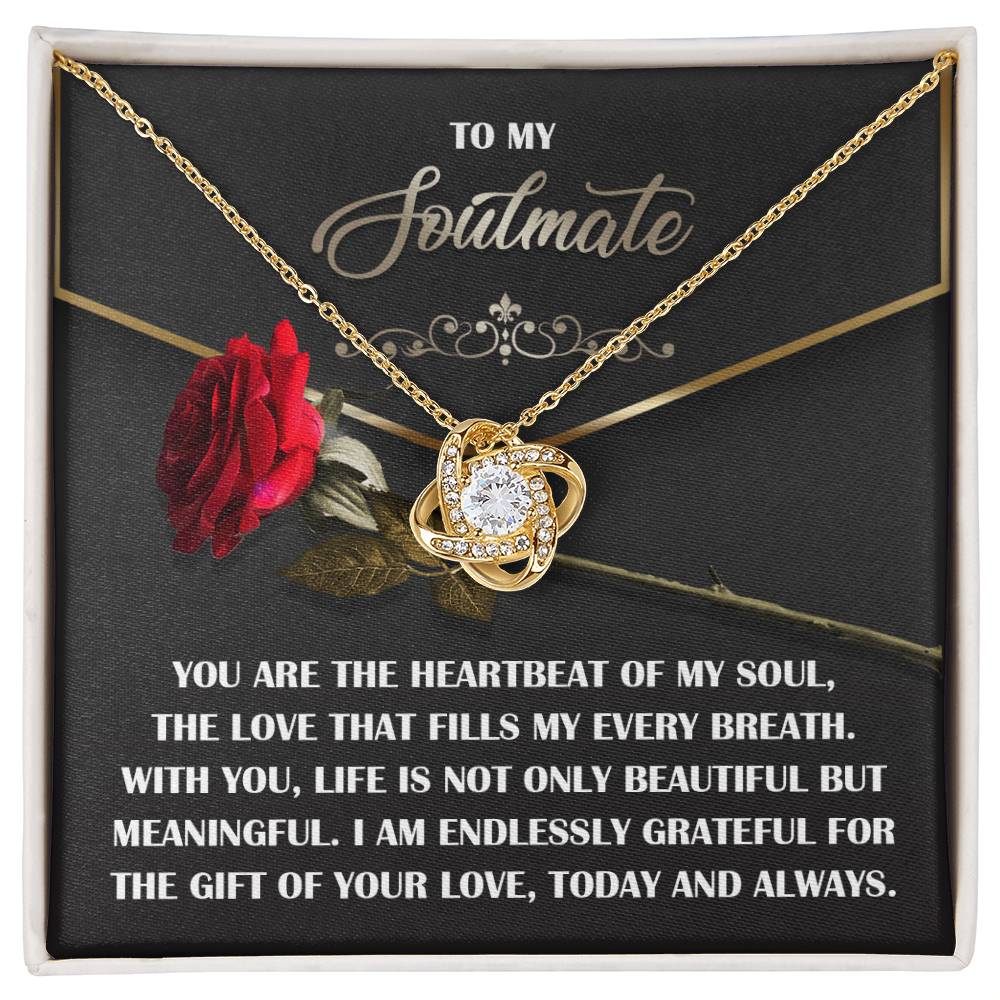 The Soulmate-My Every Breath Love Knot Necklace, featuring a central gem and shimmering cubic zirconia crystals, rests on a black card with a rose. The card reads: "To My Soulmate. You are the heartbeat of my soul... I am endlessly grateful for the gift of your love...