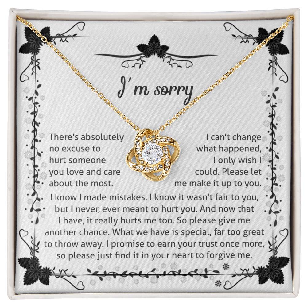 The Sorry-No Excuse - Love Knot Necklace, with a white gold finish, showcases a delicate knot design on a chain adorned with cubic zirconia crystals. The pendant is presented on a box featuring an "I'm sorry" message that expresses regret and seeks forgiveness, framed by a charming floral border at the top.