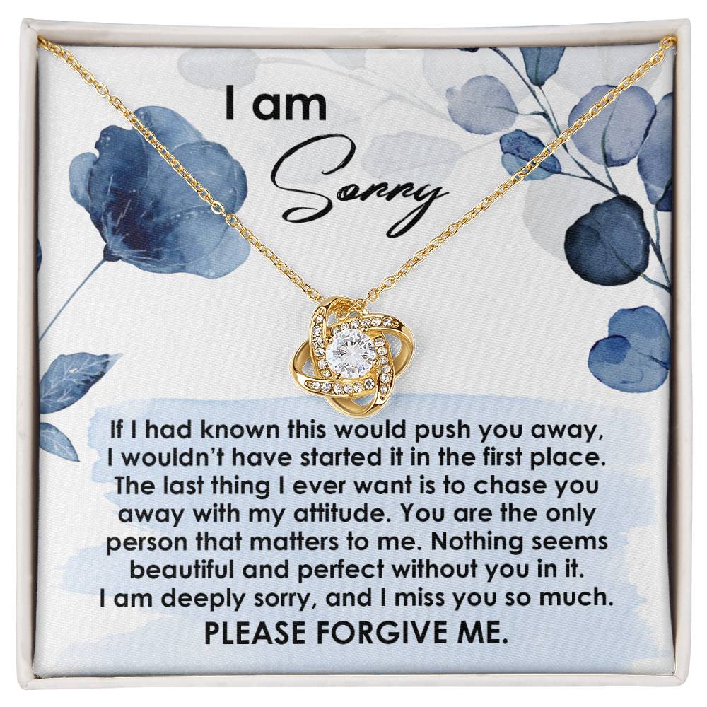 The image displays the Sorry-Push You Away - Love Knot Necklace, a stunning piece adorned with cubic zirconia crystals, nestled in a gift box. The lid of the box features an apology message along with the phrase "I am sorry" elegantly printed above the necklace. This beautiful item is available with either a white gold or yellow gold finish.