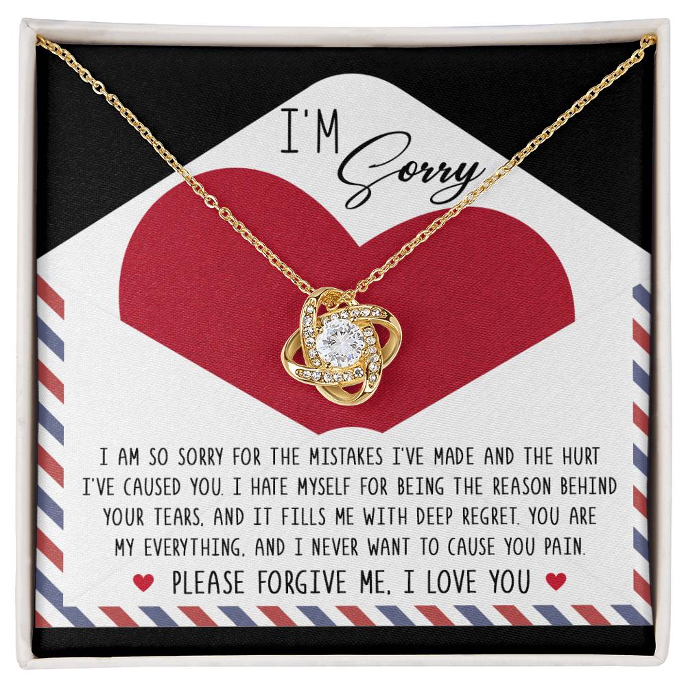 The "Sorry-Behind Your Tears" Love Knot Necklace features a gold finish and shimmering cubic zirconia crystals, beautifully presented on a card with an apology message over a red heart, expressing deep regret and asking for forgiveness, ending with the heartfelt phrase "Please forgive me, I love you.