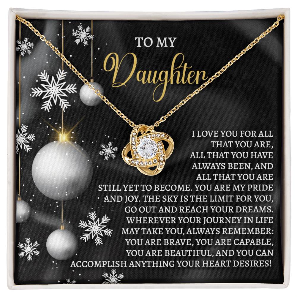 The Daughter-Pride And Joy - Love Knot Necklace, adorned with a gold pendant and enhanced with cubic zirconia, is elegantly presented on a black festive-themed card featuring a heartfelt message of love and encouragement for a daughter. This exquisite piece makes the perfect personalized gift.