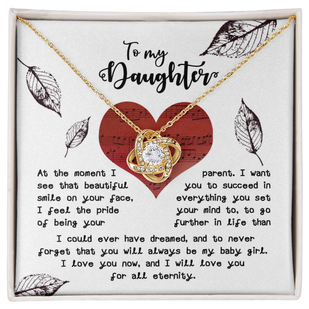 The Daughter-On Your Face - Love Knot Necklace, finished in stunning yellow gold, showcases an intertwined heart pendant adorned with sparkling cubic zirconia crystals. It comes displayed on a card that reads "To my Daughter" and includes a heartfelt message about love and encouragement.