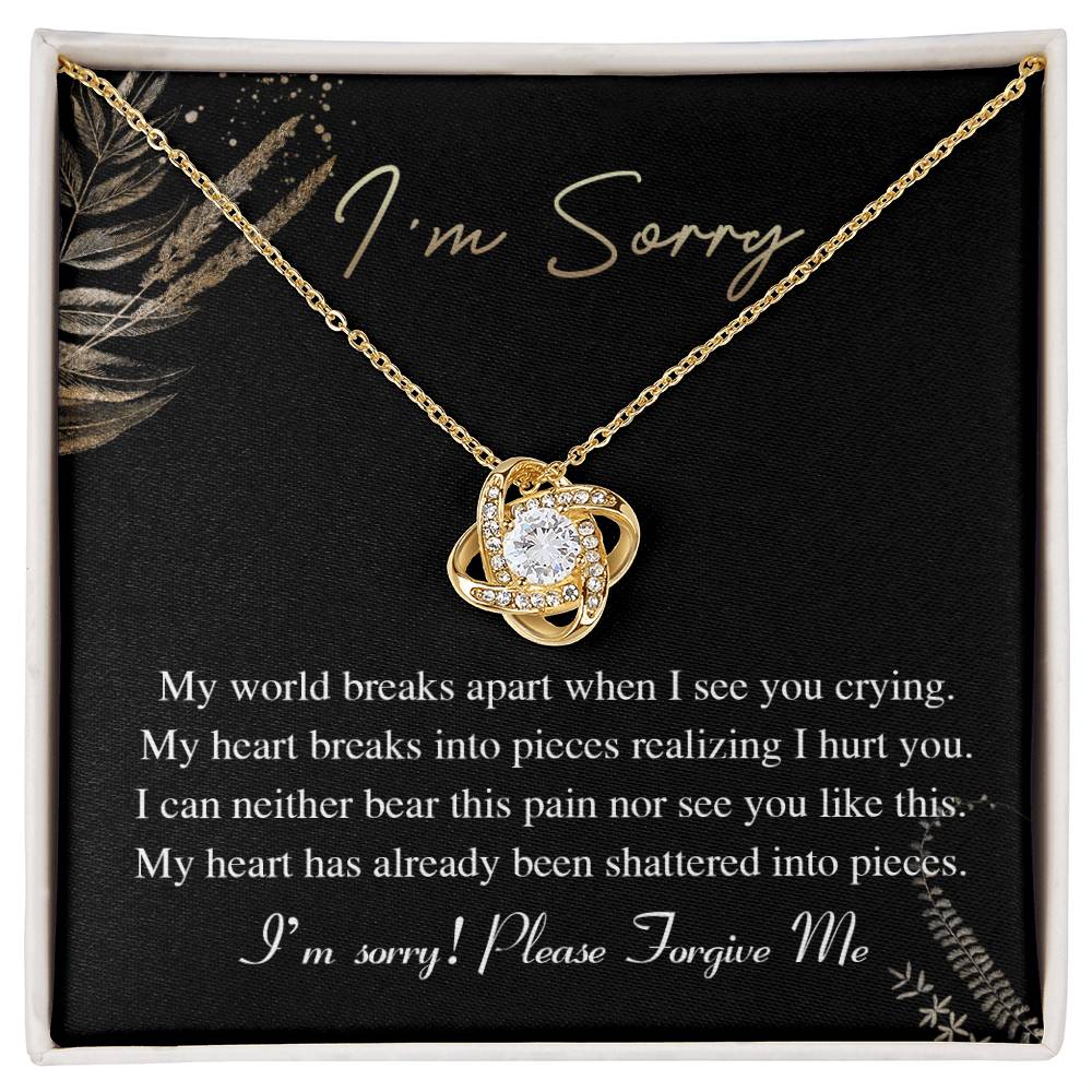 The Sorry-See You Crying - Love Knot Necklace, featuring an intertwined pendant adorned with cubic zirconia crystals, is elegantly displayed on a black card with the inscription "I'm Sorry" and an apology message in white text.