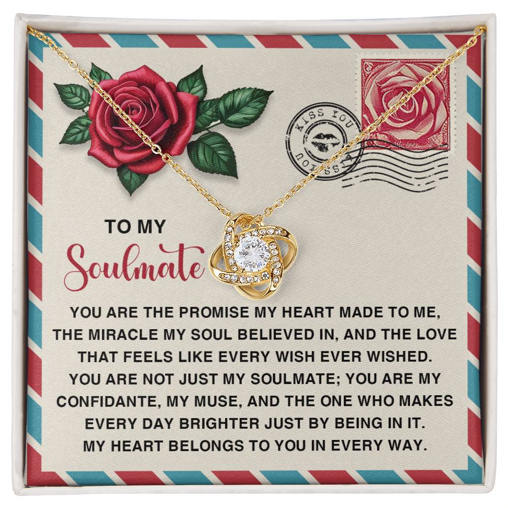 The Soulmate-Made To Me Love Knot Necklace features a gold necklace with a heart-shaped pendant in an open gift box. The box is adorned with sparkling cubic zirconia, uplifting messages about love and soulmates, plus rose and stamp illustrations—ideal for a personalized gift.