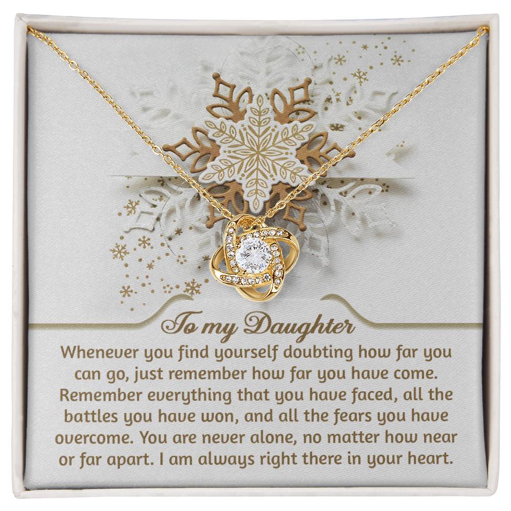 The Daughter-You Can Go - Love Knot Necklace showcases a heart-shaped pendant adorned with cubic zirconia crystals, presented on a message card that features an elegant snowflake design and an inspiring message about the unbreakable bond shared with a daughter.