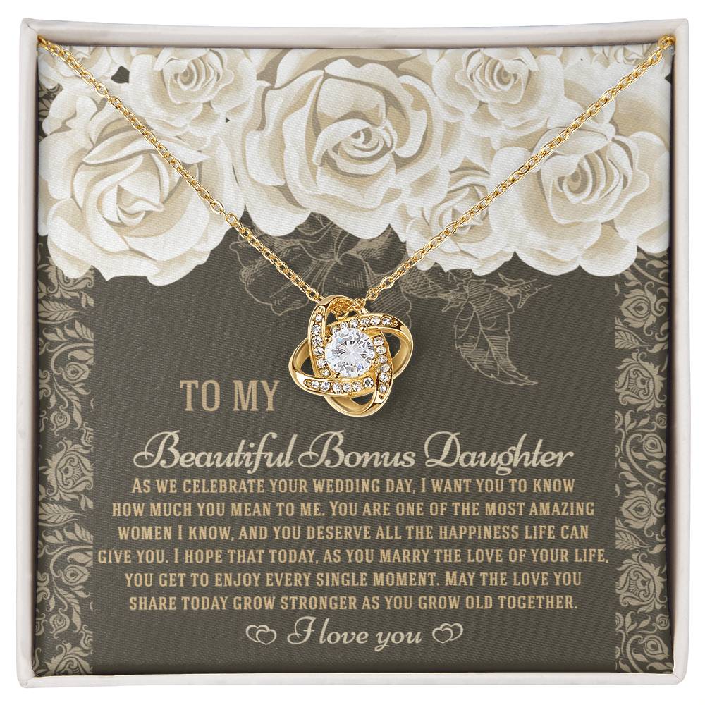 The "To Bonus Daughter, Grow Old Together - Love Knot Necklace" features a gold finish and sparkling cubic zirconia crystals. It comes packaged in a gift box decorated with an ornate floral design and includes a heartfelt message for your daughter on her wedding day.