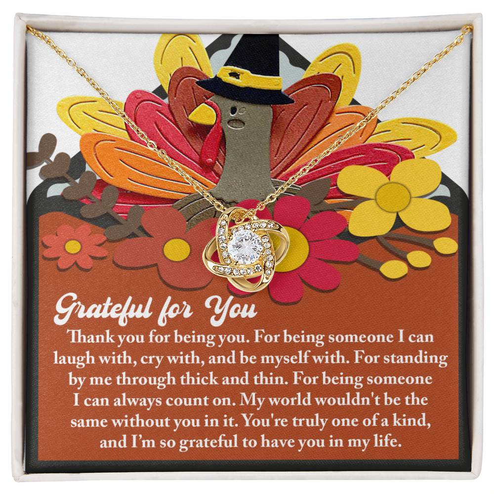 The Thanksgiving-Being You - Love Knot Necklace, adorned with sparkling cubic zirconia crystals, is gracefully displayed on a stand featuring a turkey wearing a hat and flowers. The display reads "Grateful for You," conveying heartfelt gratitude.