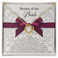 A To Bride's Mom, My New Mother - Love Knot Necklace with a heart pendant, crafted from 14k white gold and adorned with cubic zirconia crystals, is displayed on a decorative card with a maroon ribbon. The card reads, "Mother of the Bride" and contains a heartfelt message of gratitude.