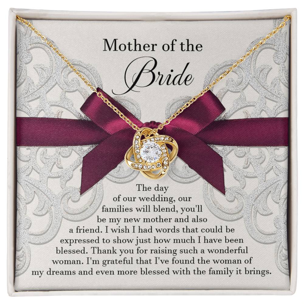 A To Bride's Mom, My New Mother - Love Knot Necklace with a heart pendant, crafted from 14k white gold and adorned with cubic zirconia crystals, is displayed on a decorative card with a maroon ribbon. The card reads, "Mother of the Bride" and contains a heartfelt message of gratitude.