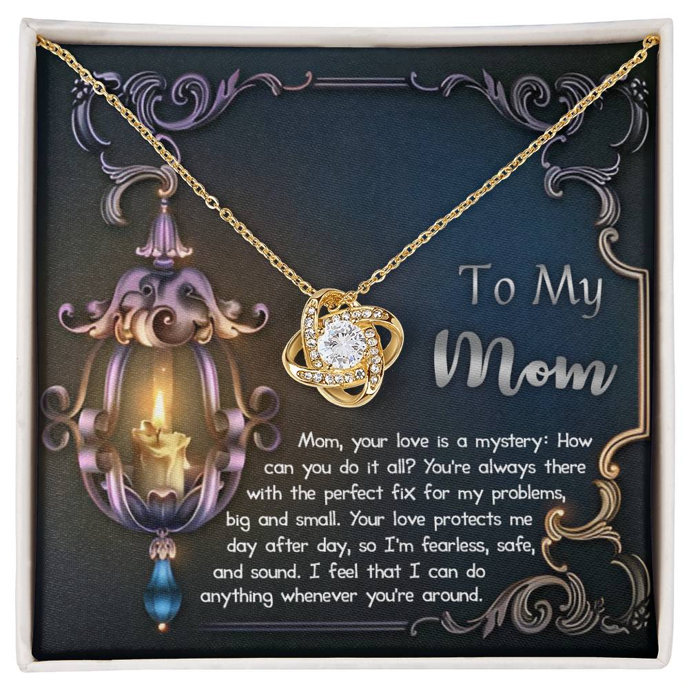 The "To Mom, Love Is Mystery - Love Knot Necklace" with a gold finish and a sparkling cubic zirconia pendant is displayed in a box. The box features a decorative background with text dedicated to a mother expressing love, gratitude, and admiration.